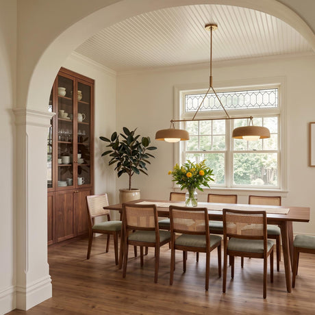 A transitional dining room with the Stratford 2 Shade Linear Pendant in aged brass and terracotta over a walnut table with cane-back chairs and a beadboard ceiling.