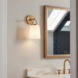 A transitional bathroom with the Stratford Wall Sconce 12", Aged Brass and Opal Glass mounted beside a wood-framed mirror above a marble vanity and navy tile.