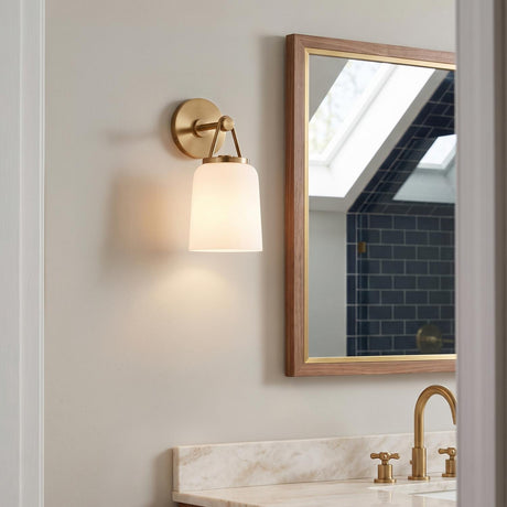 A transitional bathroom with the Stratford Wall Sconce 12", Aged Brass and Opal Glass mounted beside a wood-framed mirror above a marble vanity and navy tile.