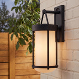 A modern home exterior with the Torrence Outdoor Wall Light in textured black and opal glass glowing on a white brick wall at twilight near a wood fence.