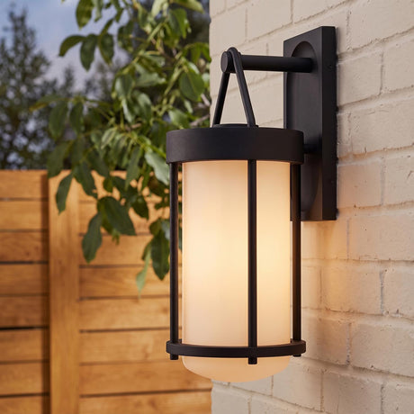 A modern home exterior with the Torrence Outdoor Wall Light in textured black and opal glass glowing on a white brick wall at twilight near a wood fence.