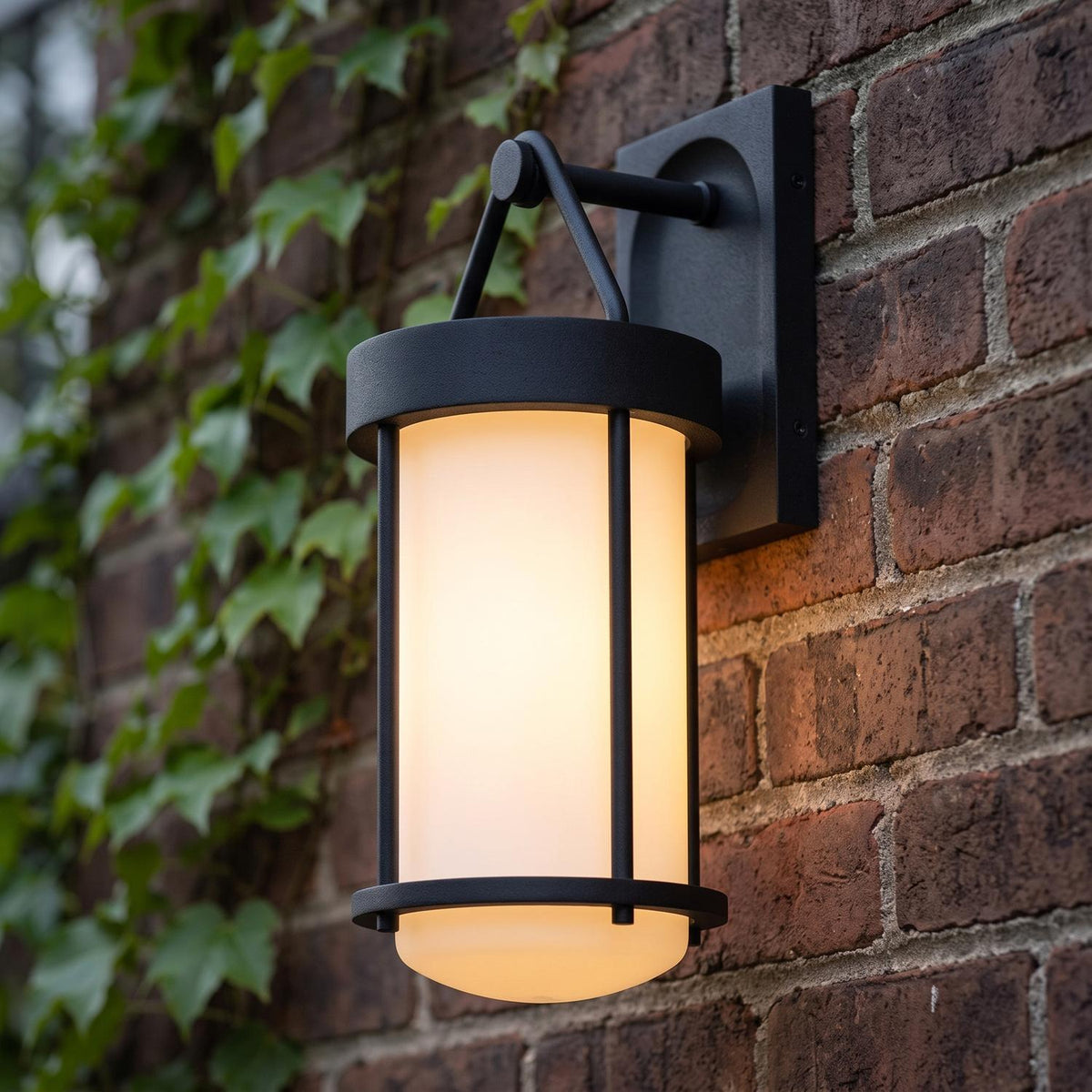 A traditional home exterior with a textured black Torrence Outdoor Wall Light with opal glass mounted on a red brick wall beside climbing green ivy at dusk.