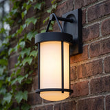 A traditional home exterior with a textured black Torrence Outdoor Wall Light with opal glass mounted on a red brick wall beside climbing green ivy at dusk.