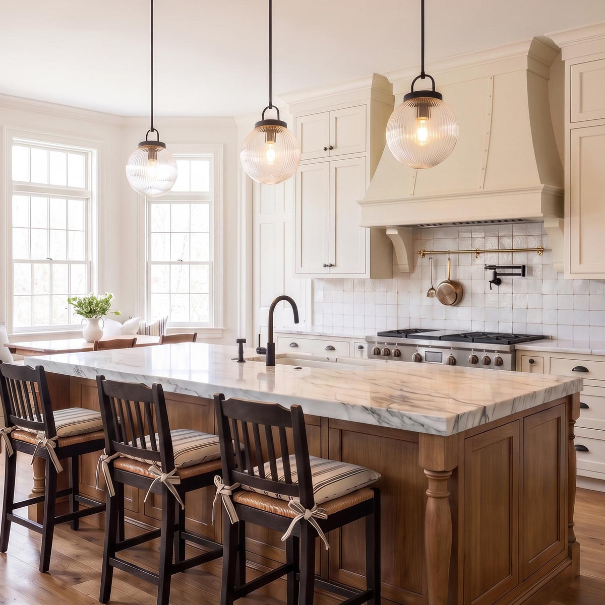 A modern farmhouse kitchen with three Whitaker Pendant 10" in matte black and clear ribbed glass over a white marble island with wood cabinetry and backsplash.