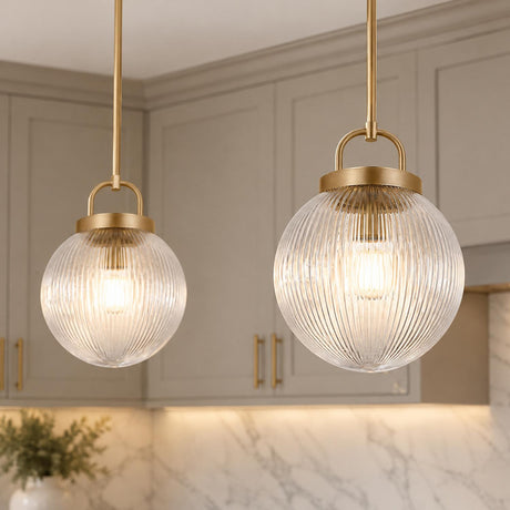 A transitional kitchen features two satin brass globe pendants with clear ribbed glass shades hanging in front of greige shaker cabinets and marble backsplash.