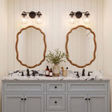 A modern farmhouse bathroom featuring two Whitaker 2 Light Vanity matte black and clear ribbed glass fixtures above scalloped wood mirrors and marble counters.
