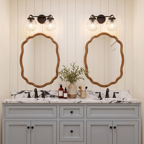 A modern farmhouse bathroom featuring two Whitaker 2 Light Vanity matte black and clear ribbed glass fixtures above scalloped wood mirrors and marble counters.