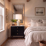 A transitional bedroom features the Stroud Large Table Lamp 27", Beige on a black nightstand beside a white upholstered bed under exposed wood ceiling beams.