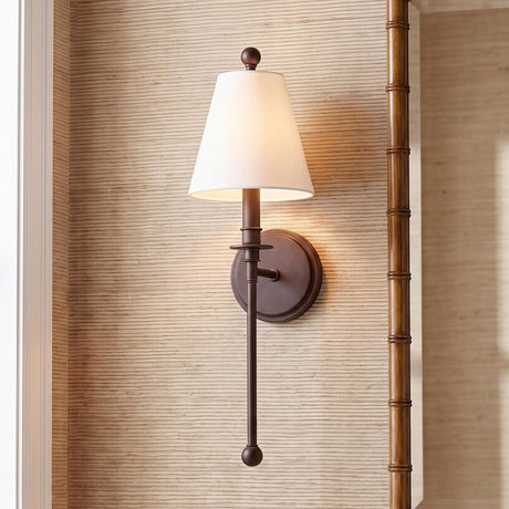 A transitional foyer with the Bellamy Wall Sconce 20", Bronze and White Fabric mounted on beige grasscloth wallpaper beside a wood bamboo-style mirror.