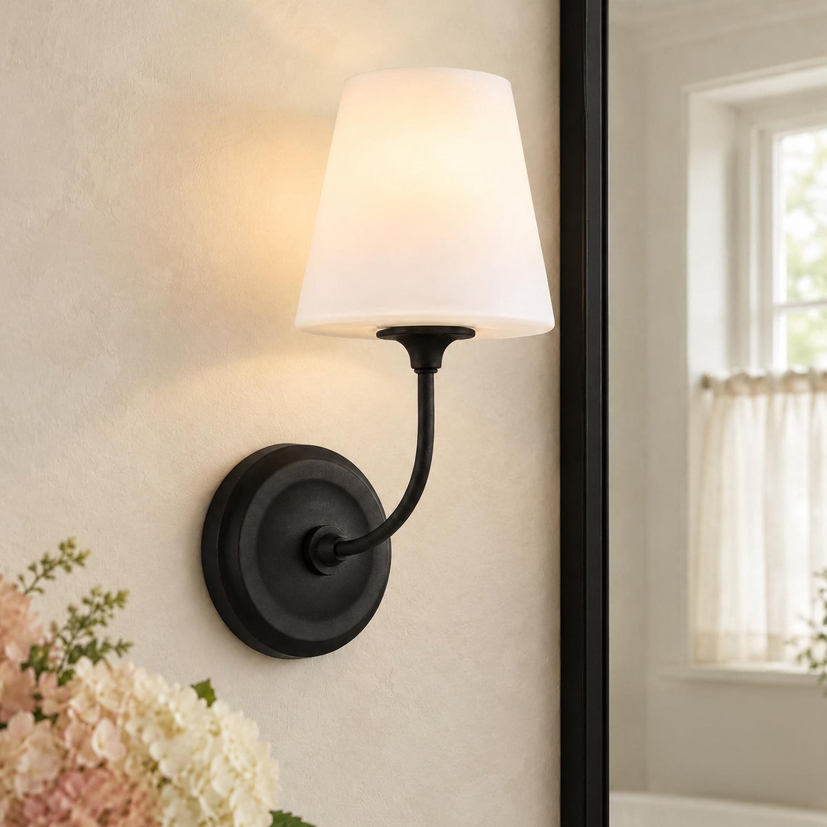 A transitional bathroom featuring the Estelle Wall Sconce 13", Forged Black and Opal Glass mounted beside a black-framed mirror on textured walls.