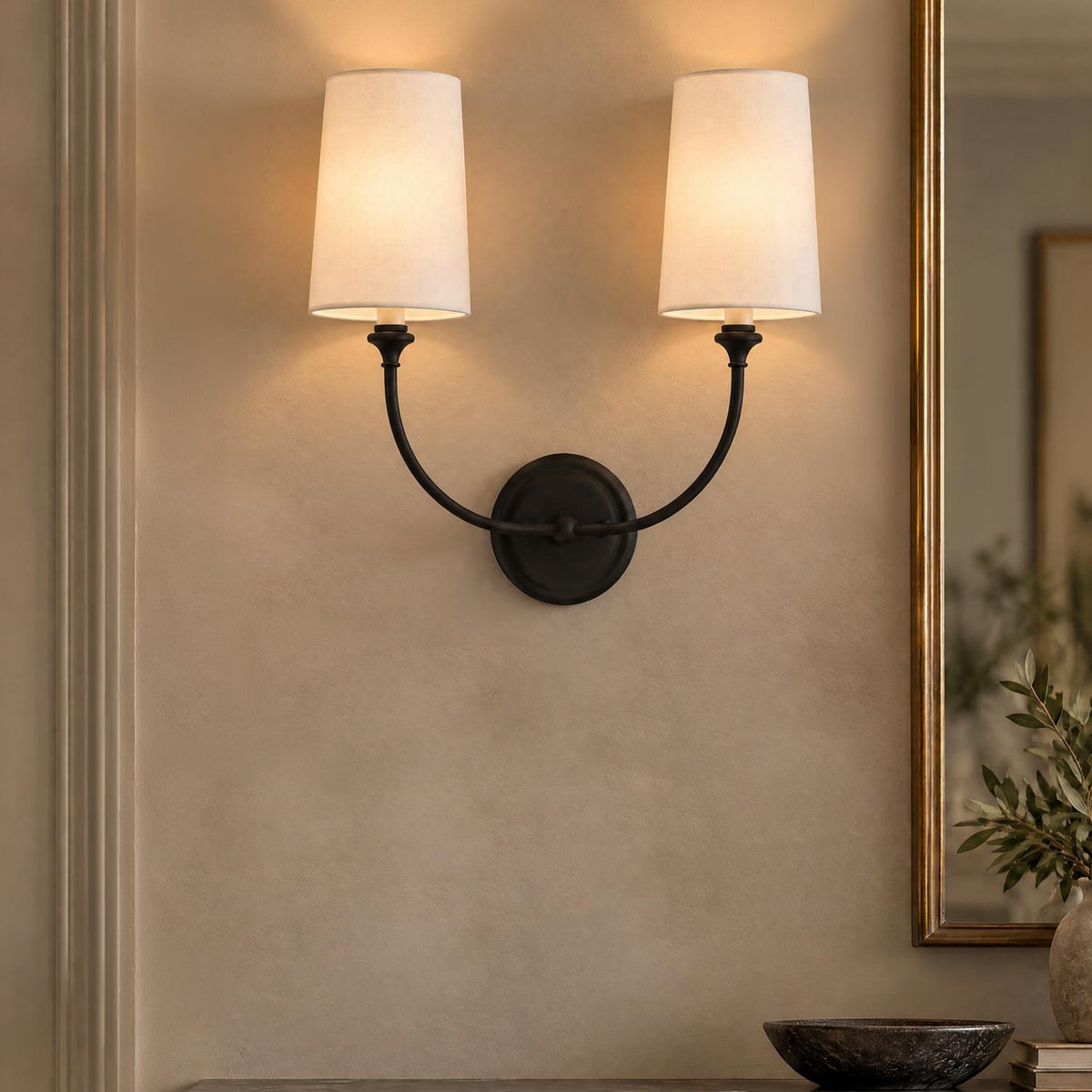 A transitional foyer featuring an Estelle Double Wall Sconce with forged black arms and white linen shades mounted beside a brass mirror.