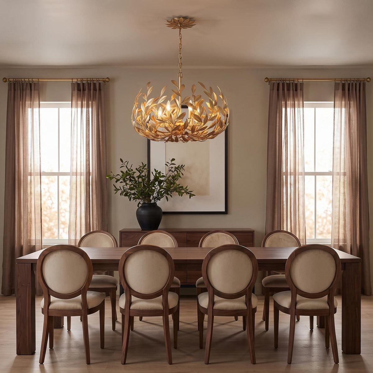 A transitional dining room features the Alison Chandelier 27", Antique Gold suspended above a long dark wood table surrounded by upholstered oval-back chairs.