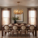 A transitional dining room features the Alison Chandelier 27", Antique Gold suspended above a long dark wood table surrounded by upholstered oval-back chairs.