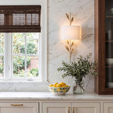 A traditional kitchen with the Alison Wall Sconce in antique gold and fabric shade mounted on a marble backsplash beside a window with dark woven blinds.