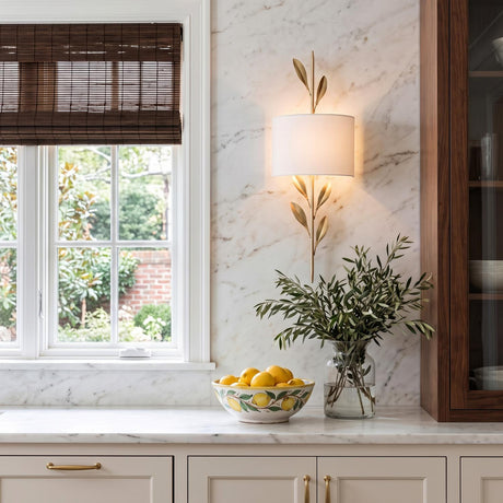 A traditional kitchen with the Alison Wall Sconce in antique gold and fabric shade mounted on a marble backsplash beside a window with dark woven blinds.