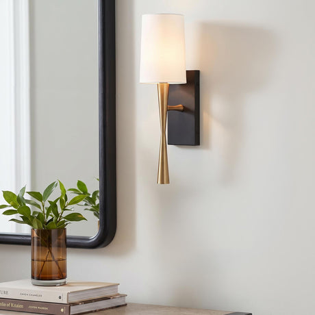 A transitional foyer featuring the Kellan Wall Sconce 18", Aged Brass and Forged Black with White Fabric shade mounted beside a black framed mirror and console table.