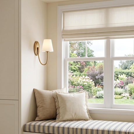A transitional bedroom nook featuring the Camira Wall Sconce in aged brass and opal glass mounted beside white built-in cabinets and a striped window seat.