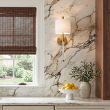 A transitional kitchen with the Bernadine Wall Sconce 22-inch, Aged Brass featuring a linen shade and glass stem mounted on a marble backsplash beside dark wood blinds.