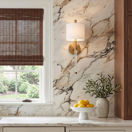 A transitional kitchen with the Bernadine Wall Sconce 22-inch, Aged Brass featuring a linen shade and glass stem mounted on a marble backsplash beside dark wood blinds.