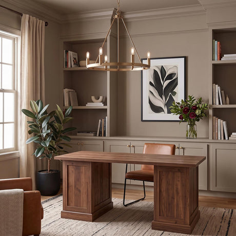 A transitional office with a satin brass chandelier centered over a wood executive desk and taupe built-in shelving with books and a rubber plant.
