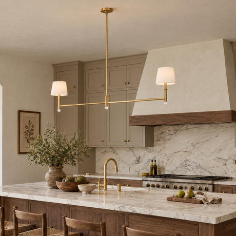 A transitional kitchen features the Savannah 2 Light Linear Pendant in gilded brass with white fabric shades over a marble island and taupe cabinets.