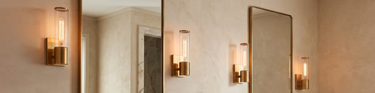 Four Lea Wall Sconces in Brass flanking two modern brass bathroom vanity mirrors.
